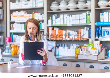 Beautiful blonde pharmacist in drugstore or pharmacy taking notes. Portrait of health care doctor in pharmacy writing on clipboard. Female pharmacist working in chemist shop or pharmacy 