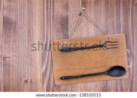 Wooden signboard with fork and spoon hanging on wall background