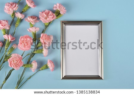 Pink carnation flowers and a vertical frame for a photo on a blue background. The concept of congratulations on the holiday. View from above.