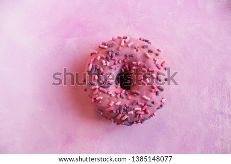 A doughnut on a pink textured background. The view from the top.