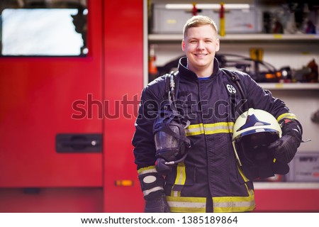 Photo of happy male firefighter with helmet in his hands against background of fire truck