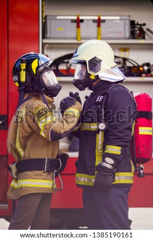 Picture of firefighters women and men in helmet and mask looking at each other and doing handshake near fire truck