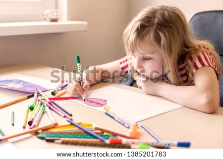 Little girl is writing a letter. Girl sitting at the desk and drawing. She wrote the word hello and does not know how to continue. Writing a letter concept. Sadness, melancholy, creative crisis. 