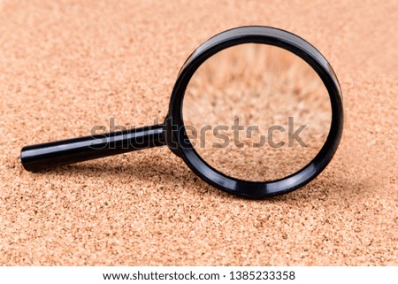 Black magnifying glass over a white and cork background