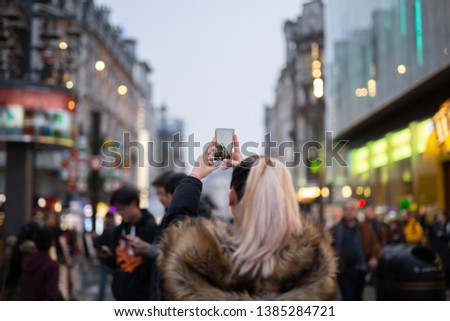 Woman tourist taking pictures of city with her cellphone in blurred background.