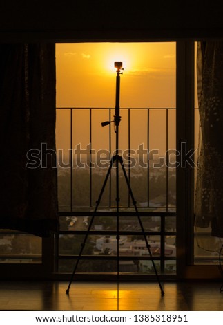 Silhouette of a action camera mounted on a tripod for taking a time lapse of a sunset or sunrise from a tall apartments balcony.  
