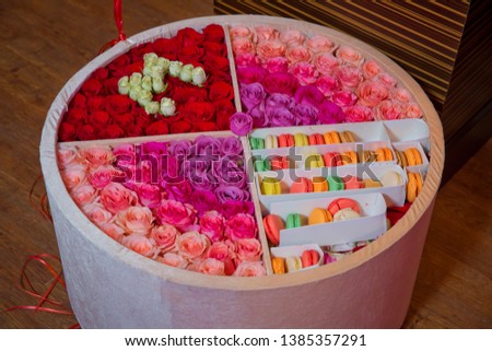 Colorful macarons cake . Paper Box with french dessert - macaroons on gray concrete table with festive decoration. Red and purple flowers