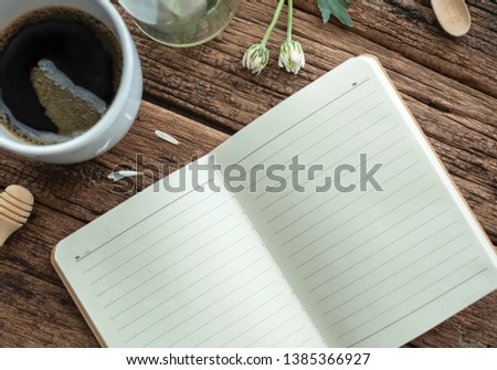 Black coffee cup with white flower& blank notebook on wood table. The morning light from window makes the house more cozy& romantic. This photo is good for chillout music cover. Lazy Sunday concept. 