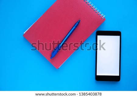 A black phone with a white screen and a pink message sign lies next to a red diary and pen on a blue background.