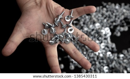 Sharp screws in hand on black background.