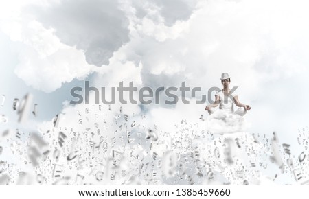 Woman in white clothing keeping eyes closed and looking concentrated while meditating among flying letters in the air with cloudy skyscape on background.