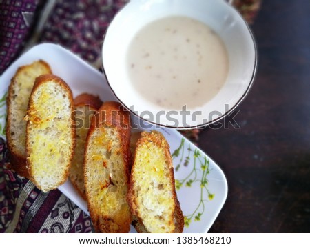 Tasty bread with garlic, cheese and herbs served with mushroom soup on the table.