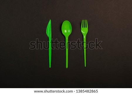 Green Disposable plastic tableware and appliances for the food on a black background. Fork, spoon and knife. Concept plastic, harmful, environmental pollution, stop plastic. Flat lay, top view.