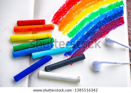 draw rainbow by chalks on notebook, earphones and colors chalks on the notebook, art style, cold design, cool colors.