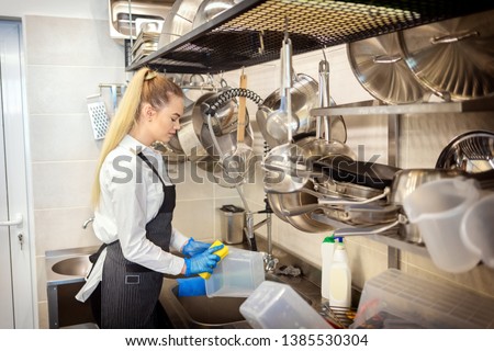 Chef of small restaurant washing dishes in sink at end of working day – kitchen worker using sponge to clean dishes – young woman at work in eatery kitchen Royalty-Free Stock Photo #1385530304