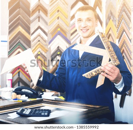 portrait of happy american  man seller working with picture frames in atelier
