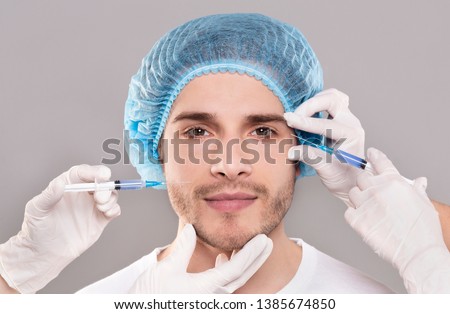 Plastic surgery concept. Man's face and beautician's hands with syringes making beauty injections, close up
