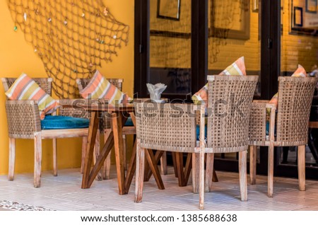 Wooden table, four wicker chairs with pillows and a wall with a decor in a cafe. Near the stained glass windows