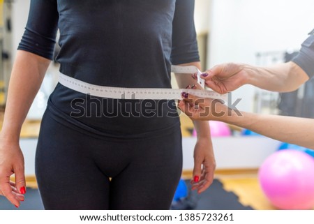 Weight lose concept with healthy woman happiness with result of workout measure tpae show number of her work hard in gym. Woman measuring her waist by measure tape after a diet over gim background