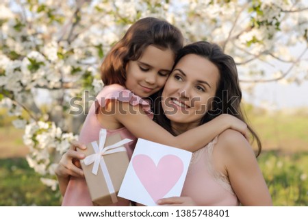 happy mother's Day! child daughter gives mom a heart card and a gift. Happy Birthday. People, holidays and family concept-happy daughter and mother against the background of blooming flowers