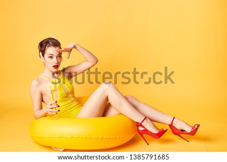 girl in a yellow bathing suit with a cocktail in her hand and a rubber ring on a yellow background