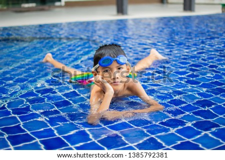 cute little boy feel happy play and swimming at swimming pool , sunny day and soft focus.
