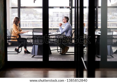 A businessman and young woman meeting for a job interview, full length, seen through glass wall Royalty-Free Stock Photo #1385852840
