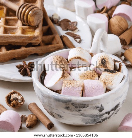 Ceramic cup of hot chocolate with marshmallow s'mores with homemade honey wafers and ingredients above over white marble table. Winter drink. Close up. Square image