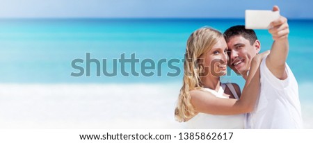 Happy couple taking a photo on a beach with turquoise sea background. Travel vacation concept. Panorama banner