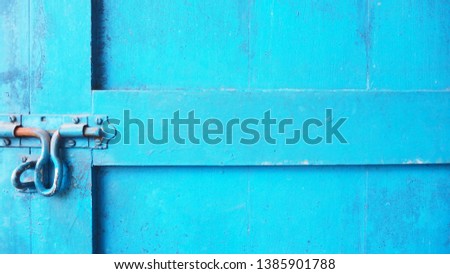 Closeup of the old and classic rusty door latch and lock on wooden bright blue painted door. Vintage decoration and lifestyle concept