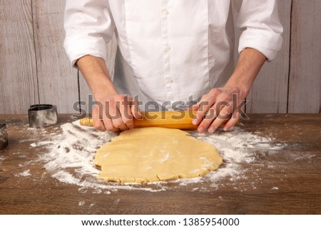 Dough preparation for cookies, pies, cakes, pizza. Hands roll out the dough with a rolling pin on a wooden table, in the kitchen closeup. Copy space, space for text