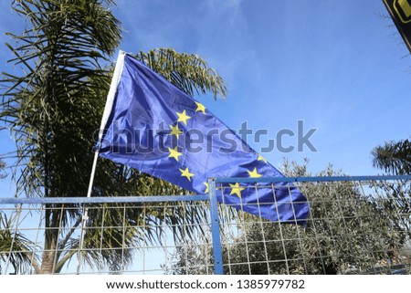 European Union flag on a background of blue sky, palm trees and an iron fence