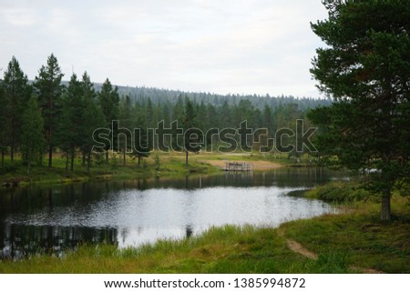 A small lake with a wooden pier,  surrounded by green trees, Saariselka, Lapland, Finland