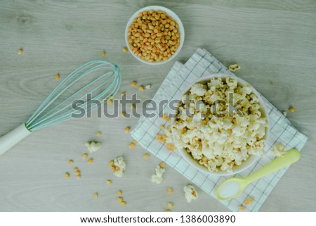 Popcorn in white bowl with pastel spoon, salt, hand mixer and corn seeds on wood background. Cooking for party