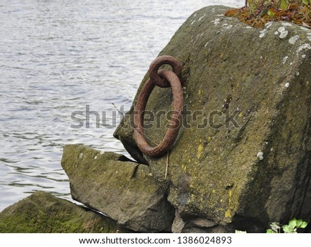 Large metal ring attached to a large stone next to water. 