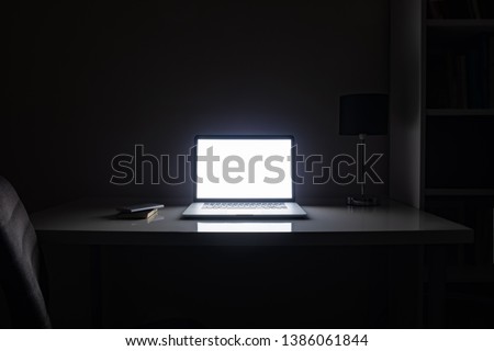Room illuminated by a computer screen at night, no people. Empty workplace lit by a laptop display in the darkness, late work, overtime concept Royalty-Free Stock Photo #1386061844
