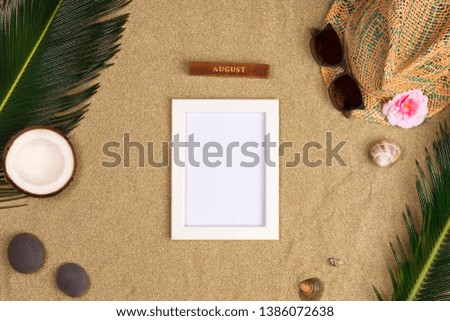 Stylish summer composition with photo frame, green leaves, hat and sunglasses on a sand background. Artwork mockup with copy space