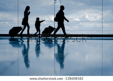 Silhouette of young family with luggage walking at airport, girl pointing at the window