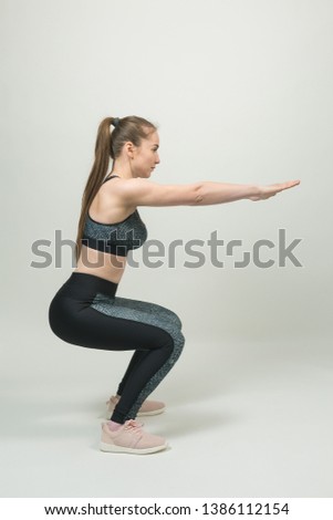 Slim fit fitness girl performs a set of exercises on a gray background. A girl in sporty tight black snake skin texture clothes