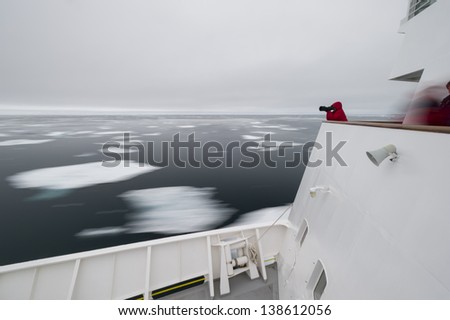 Tourist in the Arctic taking a photo while standing on top of a ship with icebergs passing by, Svalbard, Norway