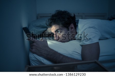 Addicted to social media young man chatting and surfing on the Internet on smart phone at night in bed. Sleepless in dark bedroom with mobile screen light. In insomnia and online network addiction. Royalty-Free Stock Photo #1386129230