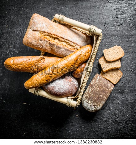 Different types of bread in the basket. On black rustic background