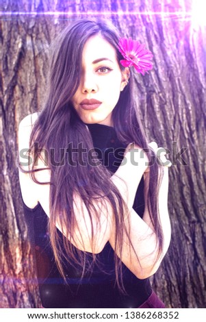 beautiful colorful bright photo with light effects of young brunette skinny Caucasian female fashion model outside on sunny day with big flower posing in front of old  tree bark in the background 