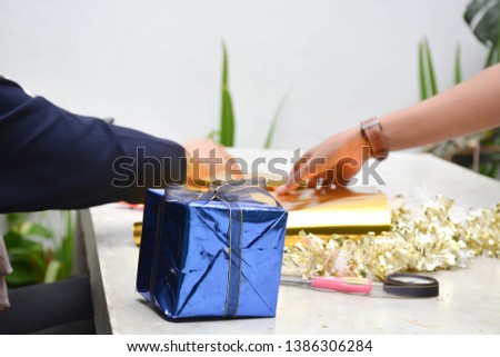 close up of body part female hand taking photograph of gift wrapping on golden and blue colour sitting on concrete table at day time -image