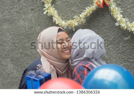 portrait of two hijab woman bestfriend having time together in celebrate birthday surprise party giving blue gift and kiss on the cheek together -image
