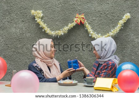 portrait of two hijab woman bestfriend having time together in celebrate birthday surprise party giving blue gift and kiss on the cheek together -image