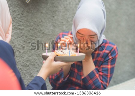 attractive hijab woman having surprise birthday cake from her bestfriend with candle while sitting on cafe -image