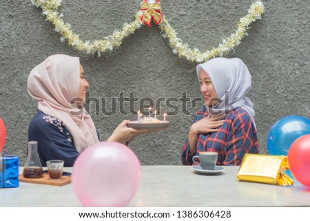 Portrait of two hijab woman bestfriend celebrate birthday with pancake and and light candle sitting on the cafe concrete table in day time -image
