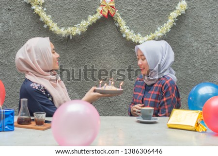 Portrait of two hijab woman bestfriend celebrate birthday with pancake and and light candle sitting on the cafe concrete table in day time -image