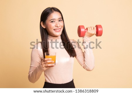 Young Asian woman with dumbbell drink orange juice on  beige background